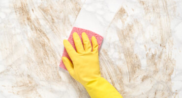 Hand wearing a glove wiping clean a dirty marble counter or floor with a sponge